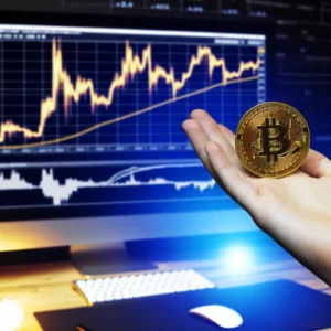 Hình ảnh bàn tay giữ đồng Bitcoin với biểu đồ tiền điện tử trên nền.